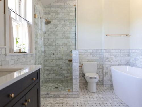 A beautifully remodeled Tulsa bathroom featuring a walk-in shower, subway tile wainscoting, a modern vanity sink cabinet, and a luxurious freestanding tub.