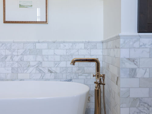A stunning Tulsa bathroom remodel featuring a freestanding tub with a floor-mounted faucet, subway tile wainscoting and backsplash, and elegant wall-mounted faucet handles.