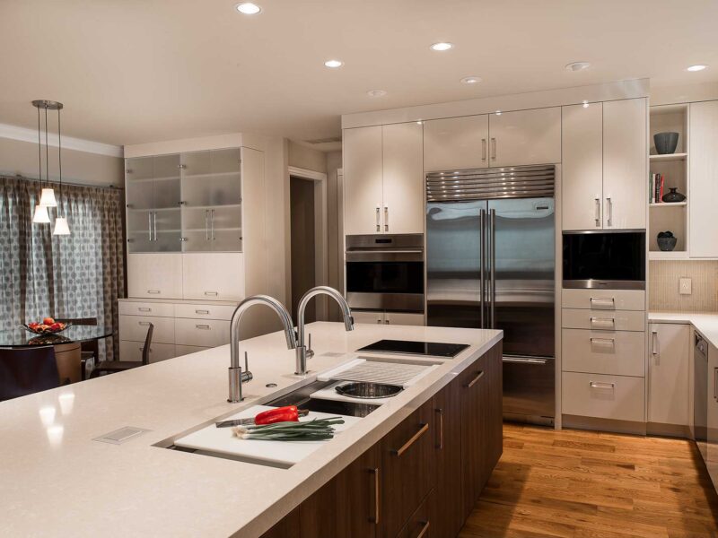Tulsa kitchen remodel featuring an island with brown cabinet storage, a Galley Workstation, a Wolf induction cooktop, quartz counters, white flat-panel cabinets, and stainless steel Sub-Zero, Wolf, and Miele appliances.