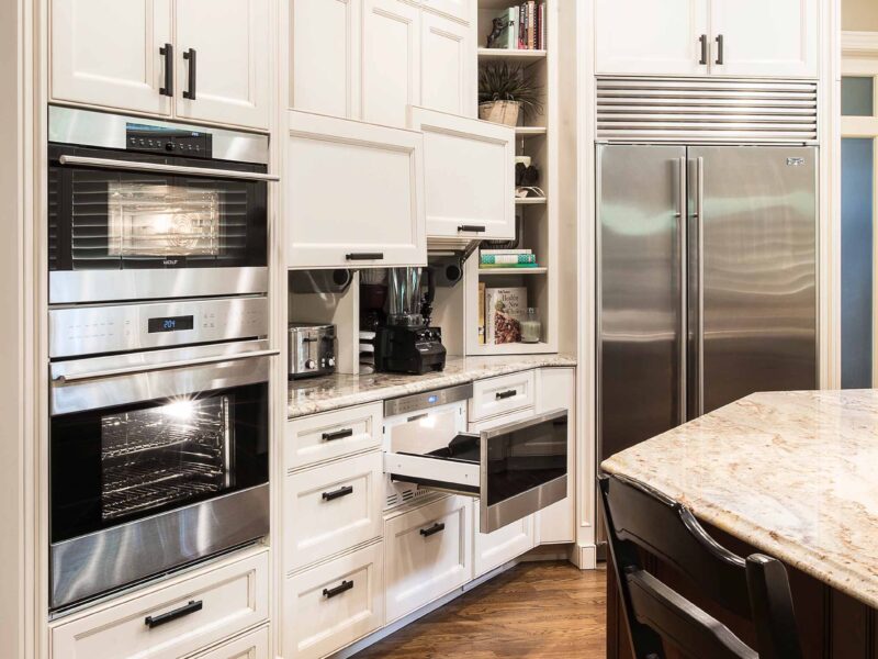 Tulsa kitchen remodel featuring kitchen drawers for appliance storage, a Wolf drawer microwave, Wolf double ovens, a Sub-Zero freezer and refrigerator, cabinet storage, a kitchen island, and wood floors.
