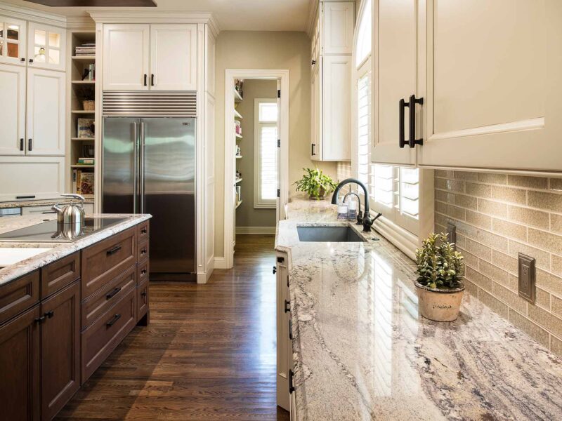 Tulsa kitchen remodel featuring an island with cabinet storage, marble countertops, a Wolf induction cooktop, an undermount sink, a subway tile backsplash, a Sub-Zero full-size freezer and refrigerator, and open shelves.
