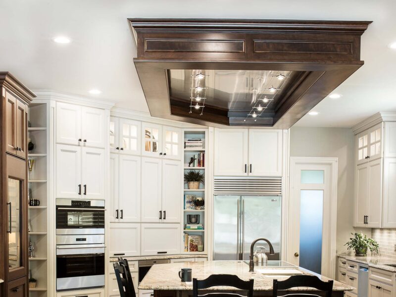 Tulsa kitchen remodel featuring a kitchen island with a vent hood, marble counters, Wolf ovens, a Sub-Zero freezer and refrigerator, open shelf storage, cream cabinets, and island seating.