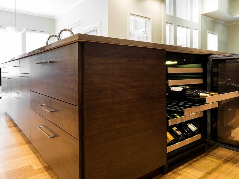Tulsa kitchen design and remodel featuring a kitchen island with a wine refrigerator, base drawer storage, and wood flooring.