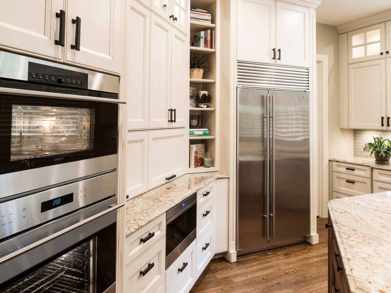 Tulsa kitchen remodel featuring tall storage, Wolf double ovens, a Wolf drawer microwave, cream painted cabinets, open shelves, and a Sub-Zero side-by-side freezer and refrigerator.