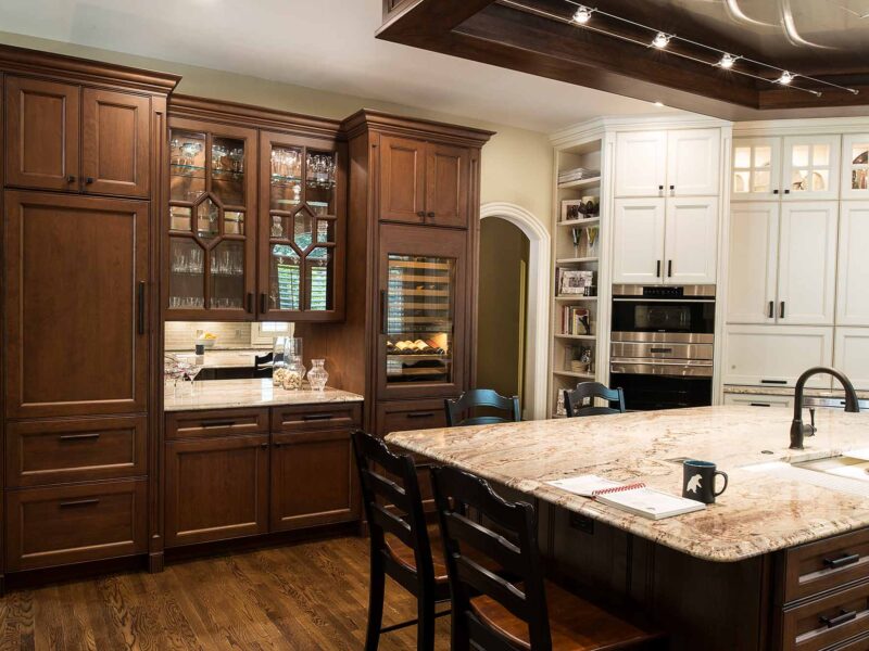 Tulsa kitchen remodel featuring a wine center, wood flooring, a large island, a ceiling vent hood, a Galley Workstation, marble counters, white tall cabinet storage, and Sub-Zero and Wolf appliances.