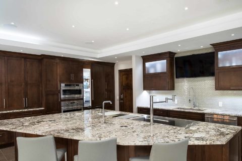 Large kitchen island seating granite counter, brown cabinet storage, undermount clean-up sink, Galley Workstation, Thermador, GE Monogram appliances, frosted glass cabinets Tulsa kitchen remodel