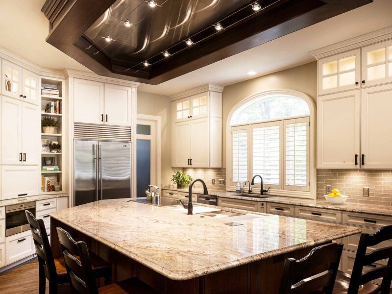 Tulsa kitchen remodel featuring a large marble counter island with a Galley Workstation, a ceiling vent hood, a Wolf induction cooktop, a Sub-Zero freezer and refrigerator, open shelves, and a Wolf drawer microwave.