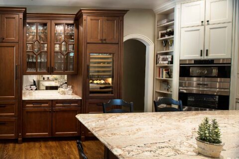 Tulsa kitchen beverage space, mirror backsplash, Sub-Zero tall wine refrigerator, brown cream cabinet storage, Wolf wall ovens, tall open shelf storage Tulsa kitchen design remodel