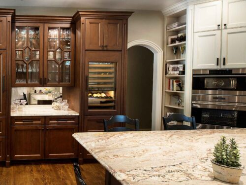 Tulsa kitchen beverage space, mirror backsplash, Sub-Zero tall wine refrigerator, brown cream cabinet storage, Wolf wall ovens, tall open shelf storage Tulsa kitchen design remodel