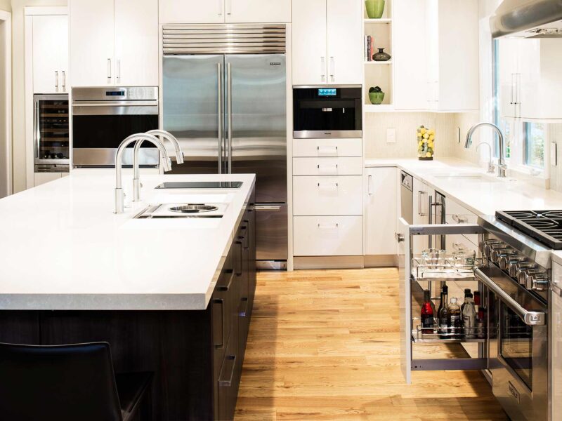 Tulsa kitchen remodel featuring white base pullout drawer storage for oils and spices, stainless steel Sub-Zero refrigerator and freezer, Wolf ovens and gas range, Miele coffee system, and a large island with a Galley Workstation.