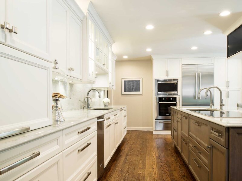 Tulsa kitchen remodel featuring white kitchen cabinets, an undermount sink, Bosch ovens, a refrigerator, a brown island with cabinet storage, and a Galley Workstation.