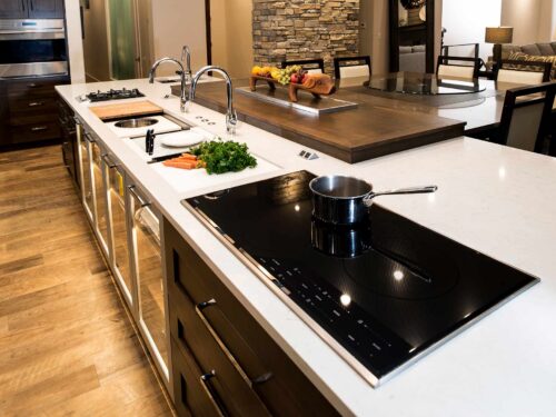 Tulsa kitchen remodel featuring a large island with storage, a Galley Workstation, a Wolf gas and induction cooktops, Caesarstone countertop, a pop-up television, and luxury vinyl wood flooring.
