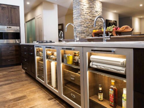 Tulsa kitchen remodel featuring an island with lit, glass base storage, a Galley Workstation large kitchen sink, Wolf convection steam ovens, and luxury vinyl flooring.