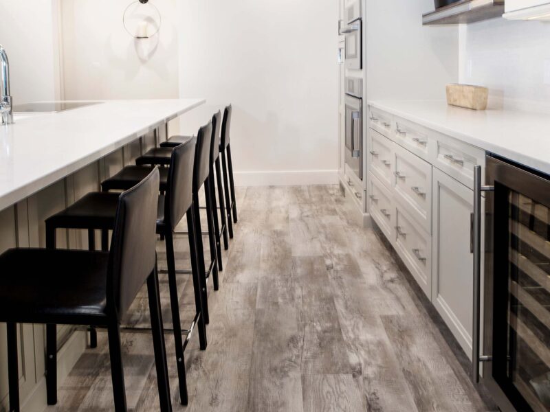 Tulsa kitchen remodel featuring a kitchen island with seating space, vinyl wood floors, white cabinet and drawer storage, a beverage refrigerator, floating shelves, and ovens.