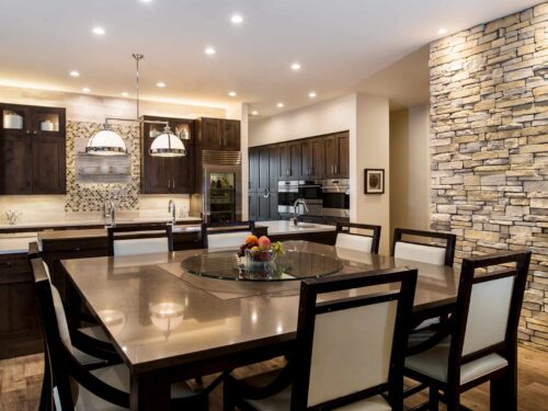 Tulsa kitchen remodel featuring a large kitchen island with a movable wood table, decorative pendants, a stone wall, Sub-Zero freezer and refrigerators, a Galley Workstation, and Wolf convection steam ovens.