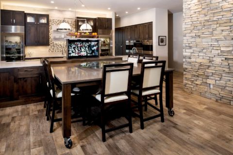 South Tulsa kitchen design and remodel featuring a movable table, a pop-up television, a large island with Caesarstone countertops, Sub-Zero and Wolf appliances, cabinet storage, and floating shelves.