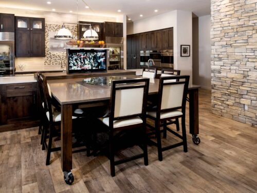 South Tulsa kitchen design and remodel featuring a movable table, a pop-up television, a large island with Caesarstone countertops, Sub-Zero and Wolf appliances, cabinet storage, and floating shelves.