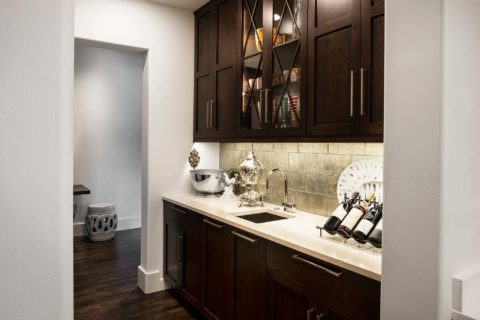 Classy Tulsa kitchen remodel walk-in bar space with decorative tile backsplash, bar sink, brown base and wall cabinet storage with glass front