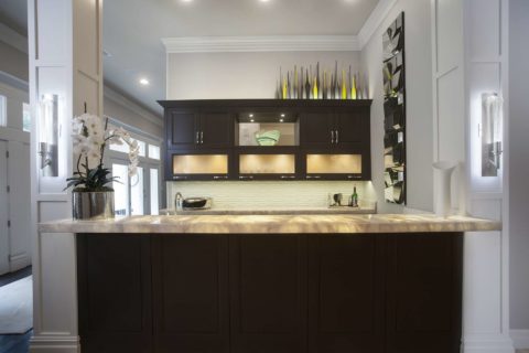 Contemporary designed and remodeled Tulsa open bar area, lit frosted glass wall cabinets, dark brown cabinet storage, glass tile backsplash and granite counters