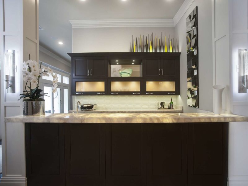 Contemporary designed open bar area featuring illuminated frosted glass wall, dark brown cabinet storage, glass tile backsplash, and granite countertops in Tulsa remodel.