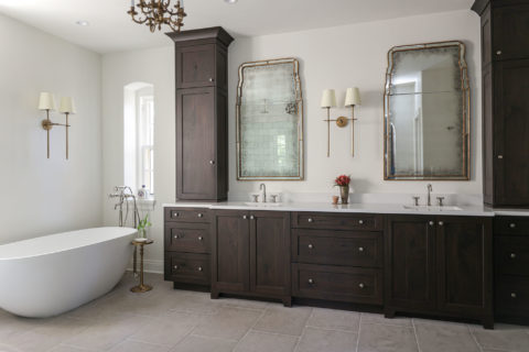 A large Tulsa master bathroom remodel featuring dual vanities, a freestanding tub, a floor-standing faucet, built-in cabinet storage, and tile flooring.