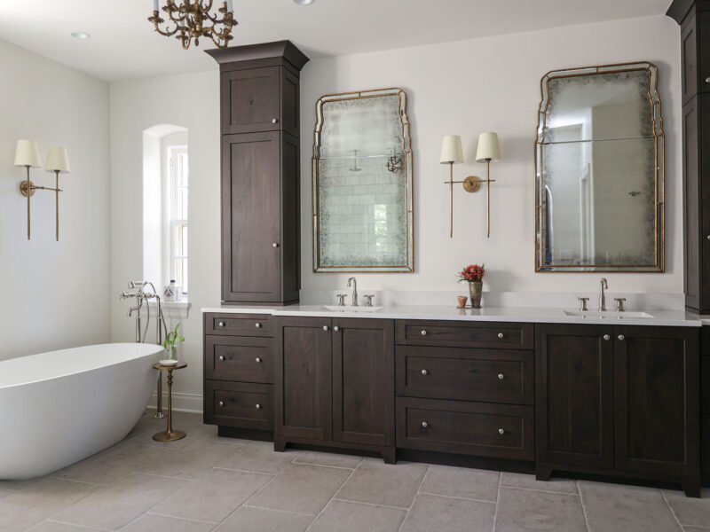 A large Tulsa master bathroom remodel featuring dual vanities, a freestanding tub, a floor-standing faucet, built-in cabinet storage, and tile flooring.
