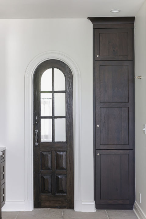 A beautiful Tulsa master bathroom remodel featuring tall storage cabinets, crown molding, a decorative ceiling, and an arched entry door.
