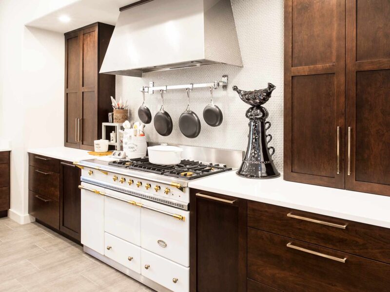 A modern kitchen remodel and design featuring a Lacanche French gas range, a vent hood, rich brown cabinet storage, a ceramic tile backsplash, and a quartz countertop.