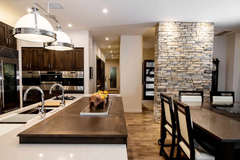 Modern south Tulsa kitchen with roll out wood table and large island with pop-up television, Caesarstone counter-top, stone wall, decorative pendant lights and Galley Workstation