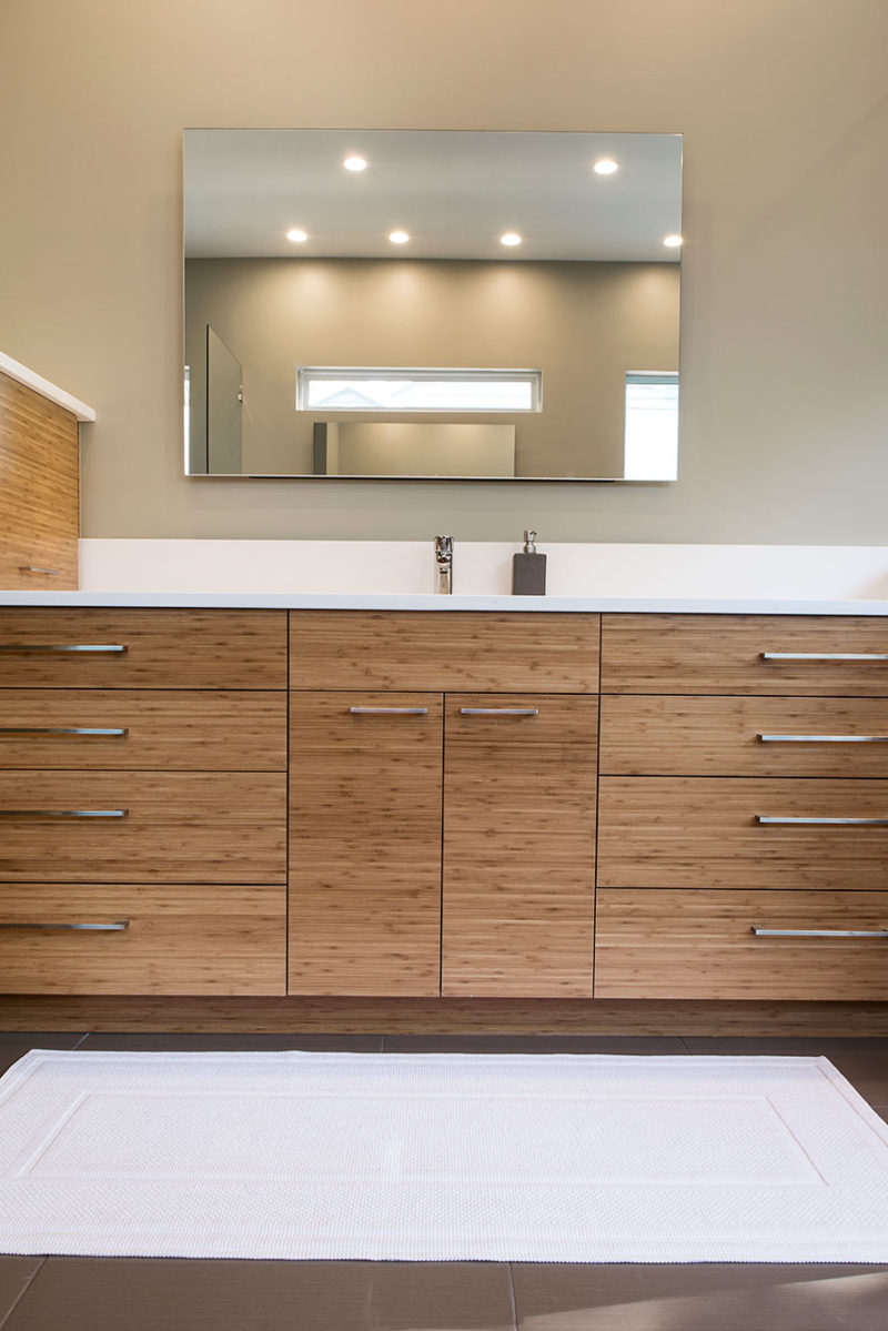 Modern Tulsa bathroom design and remodel with quartz counter and backsplash, medium brown wood grain cabinet storage, modern vanity mirror and slate gray tile flooring