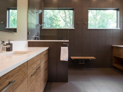 Modern Tulsa bathroom with large walk-in shower, slate gray tile walls, wood seating bench and brown cabinet vanity drawer storage