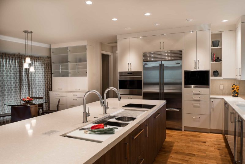 Modern Tulsa kitchen remodel island with rich brown wood cabinet storage, Galley Workstation kitchen sink, quartz counters, white cabinets, stainless Sub-Zero Wolf and Miele appliances and wood flooring