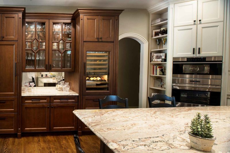 Old world Tulsa kitchen with beverage center, mirror backsplash and tall wine refrigeration in a rich brown cabinet finish, beige cabinets with stainless wall ovens and tall storage