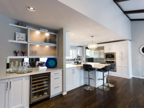 Open and functional trendy Tulsa kitchen remodel, white cabinets, stainless wine refrigerator in beverage center, frosted glass cabinets, mirror backsplash and wood floors