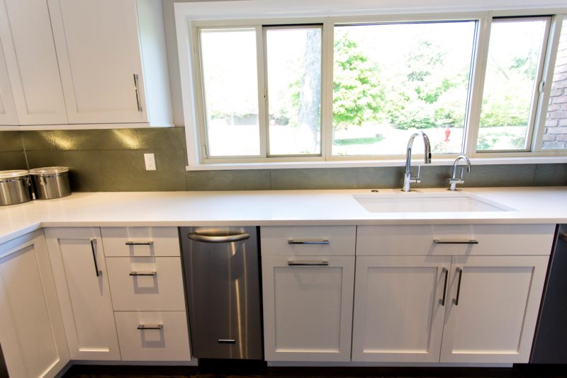 Open and functional Tulsa kitchen with white Blanco clean-up sink, stainless under counter Bosch ice maker, dishwasher, white base cabinet storage and glass tile backsplash