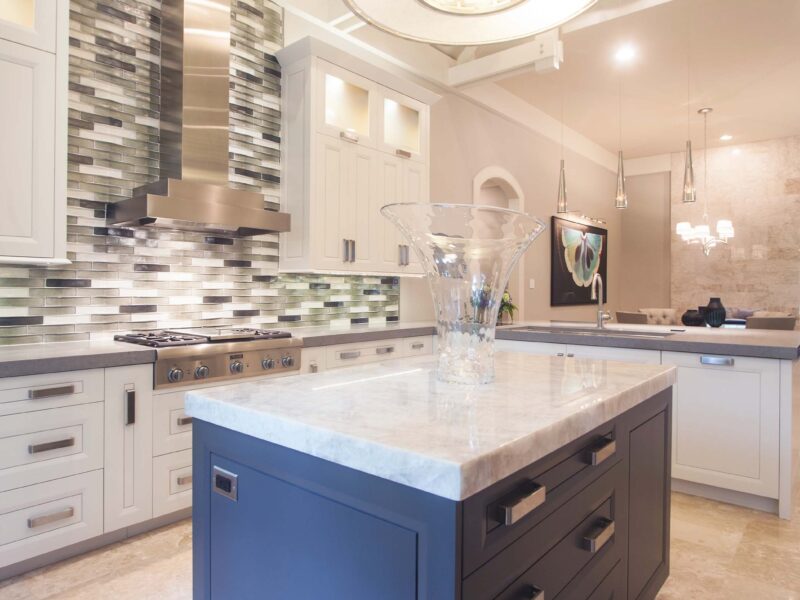 Tulsa kitchen remodel featuring a small kitchen with an island, a decorative pendant light, cabinet storage, stainless steel appliances, a vent hood, and a decorative backsplash tile.