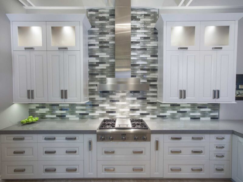 Tulsa kitchen remodel featuring a Thermador professional gas rangetop, a stainless steel canopy vent hood, a decorative subway tile backsplash, and white cabinet storage.