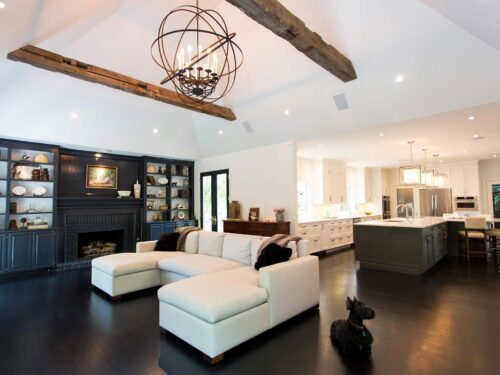 Tulsa kitchen remodel featuring an open-concept layout with an adjacent living room space, a large island, pendant lights, ceiling beams, vinyl floors, and open storage.