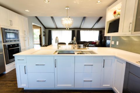 Tulsa kitchen design featuring a peninsula with storage, quartz counters, a Galley Workstation, white base cabinet storage, wood floors, a pendant light, and a Bosch French door refrigerator and freezer with a wall microwave and oven.