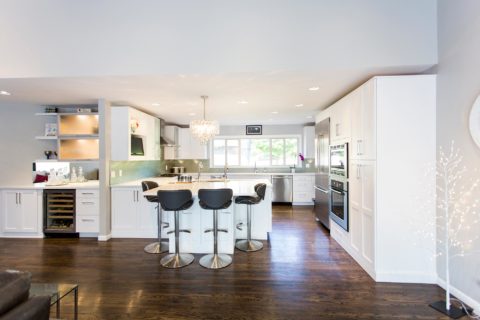 Tulsa kitchen remodel featuring an open kitchen beverage space with white cabinet storage, a bar refrigerator, frosted glass wall cabinets, a decorative pendant light, and peninsula seating.