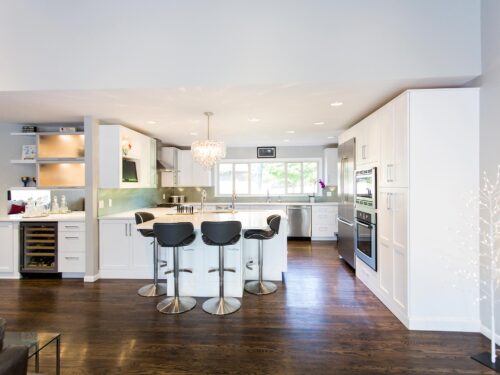 Tulsa kitchen remodel featuring an open kitchen beverage space with white cabinet storage, a bar refrigerator, frosted glass wall cabinets, a decorative pendant light, and peninsula seating.