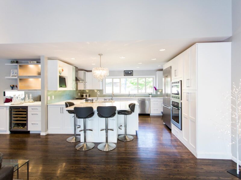 Tulsa kitchen remodel featuring an open kitchen beverage space with white cabinet storage, a bar refrigerator, frosted glass wall cabinets, a decorative pendant light, and peninsula seating.