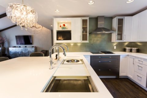 Tulsa kitchen design and remodel featuring an open kitchen with a Galley Workstation, a pendant light, Bosch induction and gas cooktops, a Bosch canopy vent hood, warming drawers, a subway tile backsplash, and white cabinet storage.