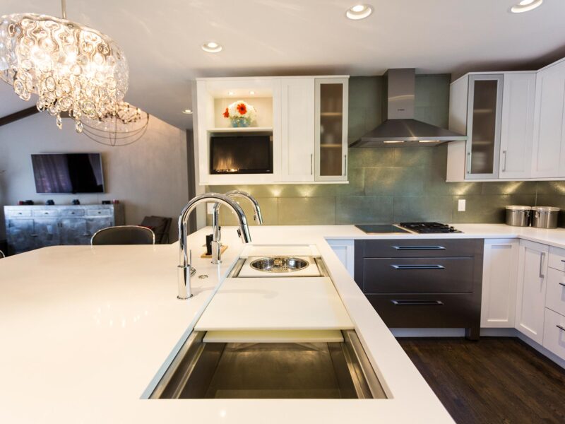 Tulsa kitchen design and remodel featuring an open kitchen with a Galley Workstation, a pendant light, Bosch induction and gas cooktops, a Bosch canopy vent hood, warming drawers, a subway tile backsplash, and white cabinet storage.