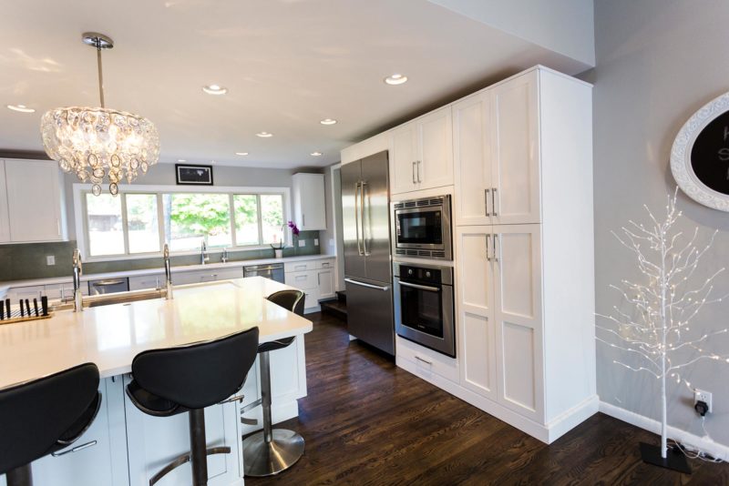 Open white Tulsa kitchen with tall pantry storage, Bosch french door refrigerator freezer, microwave oven, peninsula seating, pendant light, wood flooring Tulsa kitchen remodel