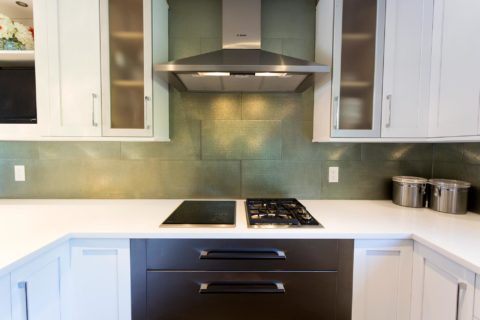 Tulsa kitchen remodel featuring a white kitchen design with Bosch two-burner induction and gas cooktops, warming drawers, a Bosch stainless steel vent hood, a glass subway tile backsplash, and wall cabinet storage.