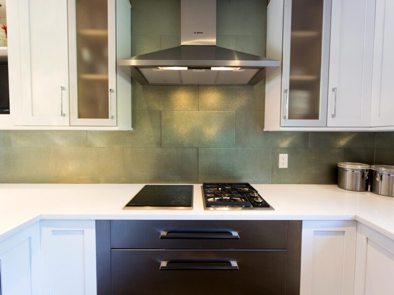 Tulsa kitchen remodel featuring a white kitchen design with Bosch two-burner induction and gas cooktops, warming drawers, a Bosch stainless steel vent hood, a glass subway tile backsplash, and wall cabinet storage.
