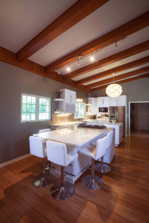 Kitchen remodel in Tulsa, Oklahoma, featuring a peninsula with seating, vaulted ceilings, a pendant light, white countertops, open shelves, a gas cooktop, and wood floors.