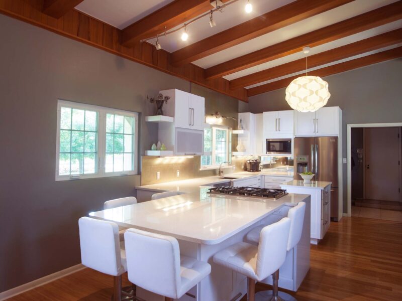 Kitchen remodel in Tulsa, Oklahoma, featuring a peninsula with seating, vaulted ceilings, a pendant light, white countertops, open shelves, a gas cooktop, and wood floors.