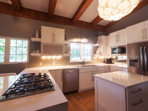 Tulsa kitchen remodel featuring an open white kitchen with vaulted ceilings, a peninsula with seating, open shelves, a stainless steel dishwasher and microwave, and a side-by-side refrigerator with a bottom freezer.